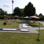Minigolfanlage bei Sonnenschein mit Sonnenschirmen und Klappstühlen zwischen den Bahnen.