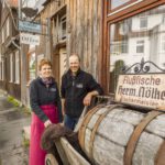 Zwei Personen stehen vor dem Laden des Fischereibetriebs Nölke und einem antiken Ladenschild.