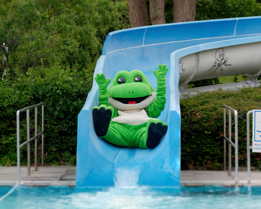 Fiete, das Frosch-Maskottechen der Stadtwerke Celle, rutscht eine Rutsche im Freibad runter