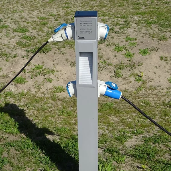 Ein Mast mit vier Steckdosen für die Wohnmobile. Zwei Stecker stecken in den Steckdosen.