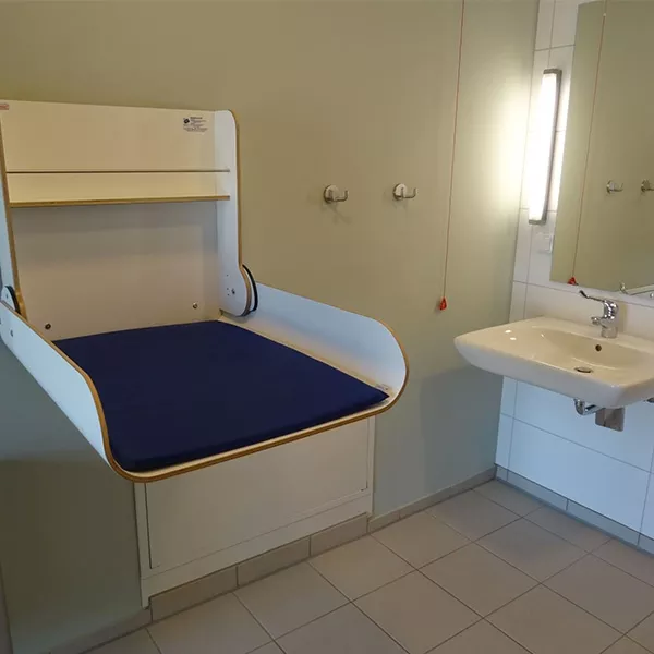 Ein Waschraum mit klappbaren Wickeltisch, Waschbecken und einem Spiegel.