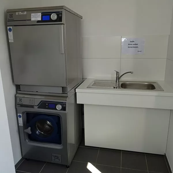 Eine Waschmaschine und ein Trockner aufeinander gestapelt. Daneben ein Edelstahlwaschbecken.