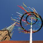 Ein Maibaum mit bunten Bändern von unten Fotografiert mit einem Kirchturm im Hintergrund.