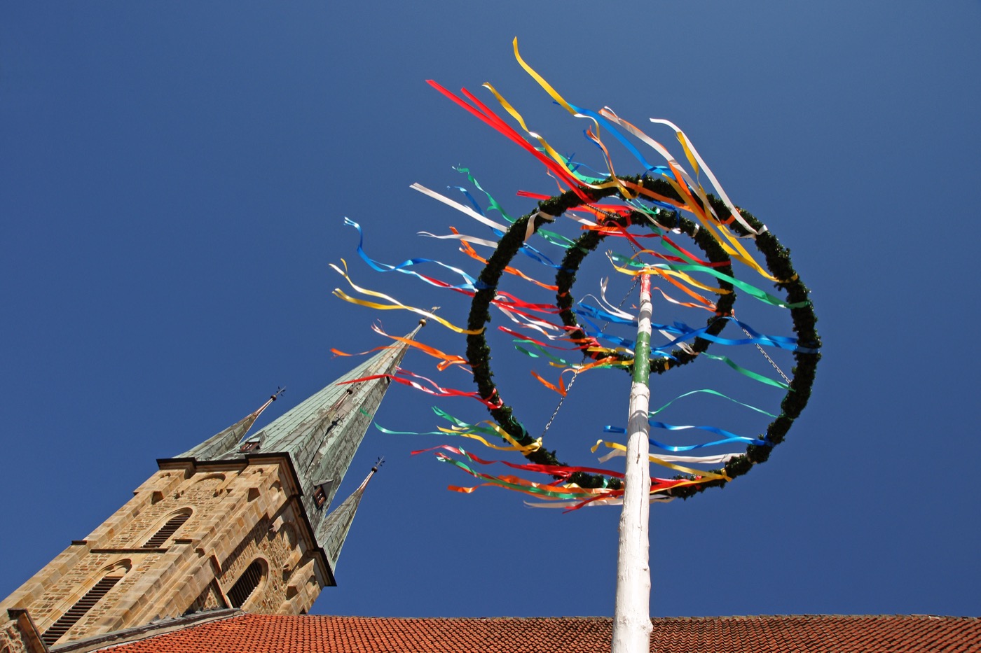 Ein Maibaum mit bunten Bändern von unten Fotografiert mit einem Kirchturm im Hintergrund.
