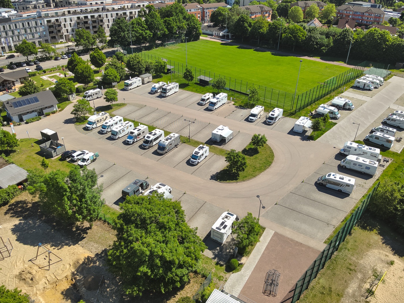 Luftaufnahme vom Wohnmobilstellplatz mit Sicht auf die Stellplätze und das Servicehäuschen und den Sportplatz